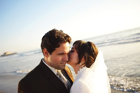 The bride whispers into the groom's ear as they share a moment on the beach, right by the ocean, after their wedding in Los Angeles
