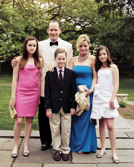 A family poses for a portraits, wearing colorful dresses; one girl wears bright pink, another a cute white dress, their mom wears a blue gown, while the father sports a tuxedo and the son a coat and tie