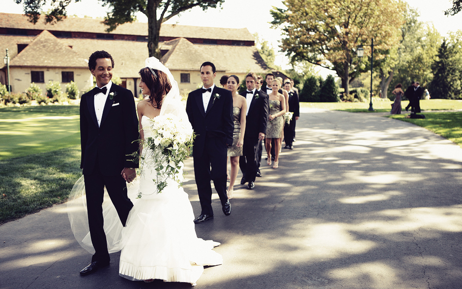 The bride and groom walk along the golf course, followed by their bridal party