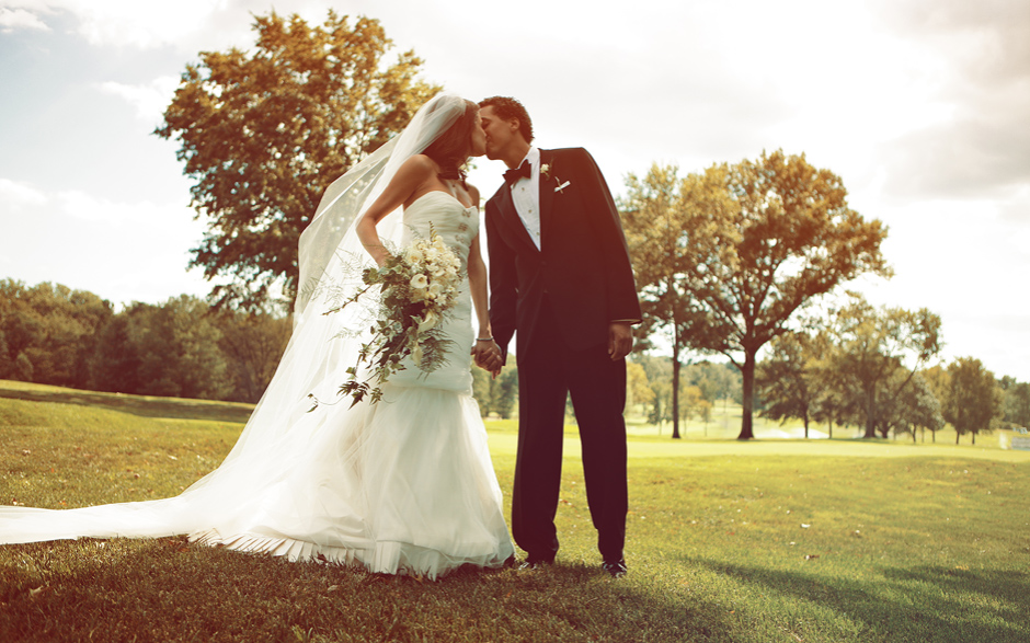 The bride and groom hold hands and kiss on the golf course on a beautiful sunny autumn day