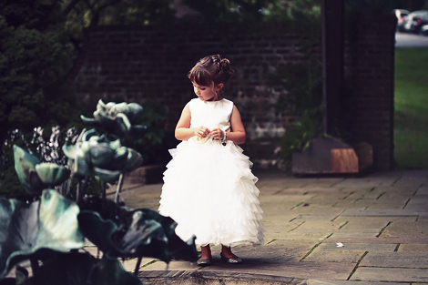The flower girl, wearing a ruffled white dress, looks into the pond and fountain at Greenville Country Club