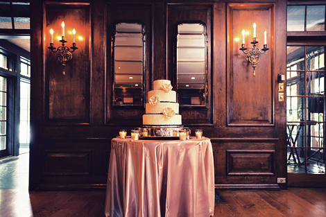 This beautiful wedding cake is adorned with white flowers and surrounded by candles at Greenville country Club, photography by Peter Van Beever