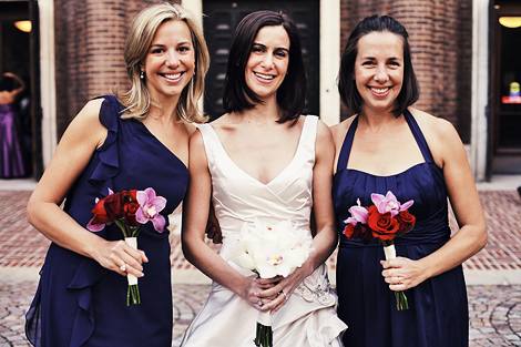 The bride poses with her bridesmaids, wearing navy blue and purple gowns, holding flowers, outside the Penn Museum of Anthropology in Philadelphia