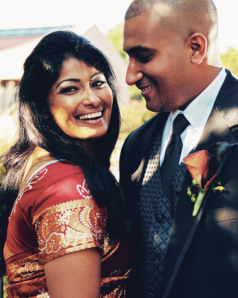 An Indian bride and groom combine the traditional with the modern; the bride wears a beautiful red sari with crystal flower details, the groom wears a vest and boutonniere