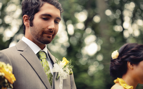 A groomsen in a green tie and yellow flower boutonniere with trees behind him.
