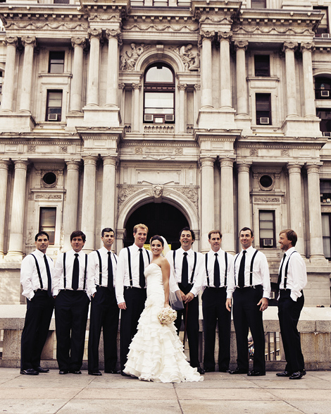 The bride and groom pose in front of City Hall in Philadelphia along with the groomsmen who wear suspenders and black ties.