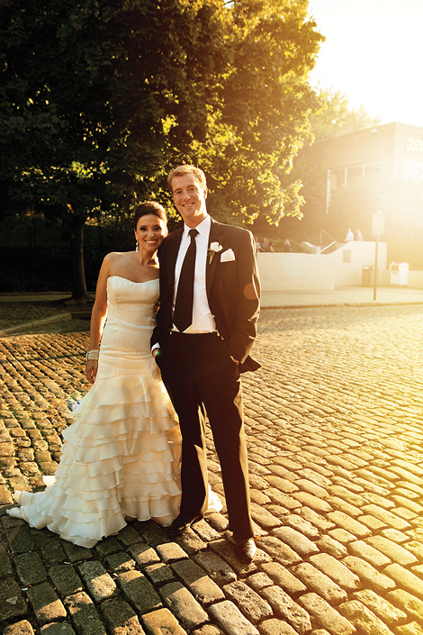 A bride and groom pose at sunset on a cobblestone street in old town Philadelphia. The groom wears a white boutonniere and hankerchief. 