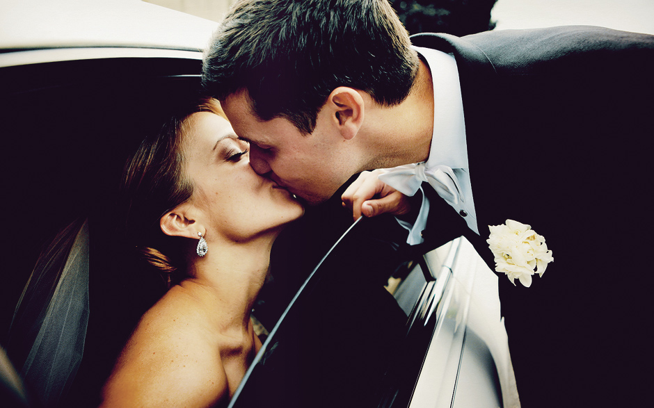A groom leans in for a kiss through the window of the limo before the bride walks down the isle. White bow tie and veil.