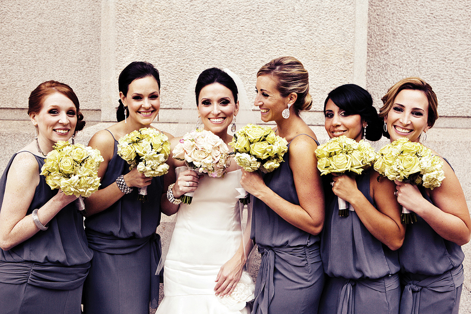The bride poses with her bridesmaids, wearing gray dresses, outside city hall in Philadelphia against the building.