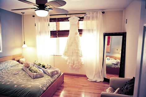 Flowers on the bed and a hanging wedding gown in the window await the bride before the ceremony