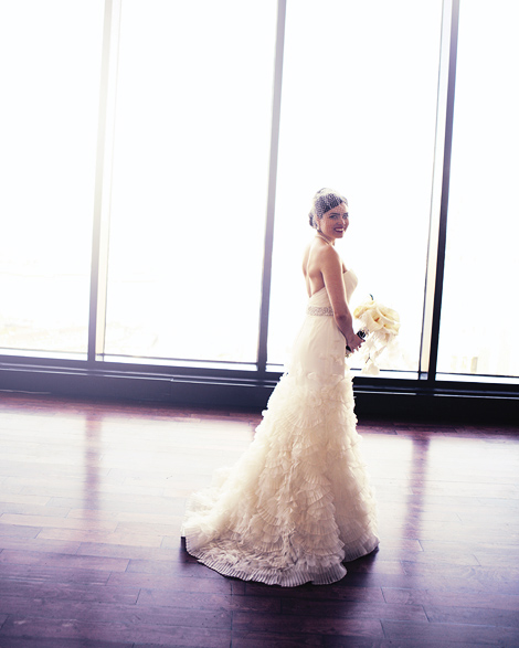 The bride poses in front of the floor to ceiling glass windows at the State Room in Boston before her wedding