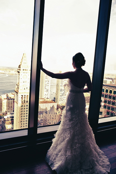The bride looks out at downtown Boston, the harbor, and clock tower from the State Room, photographer Peter Van Beever