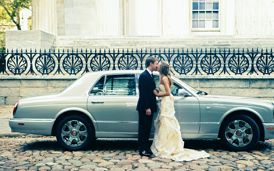 The bride and groom kiss in front of a Bentley and the bank building on their wedding day in Philadelphia