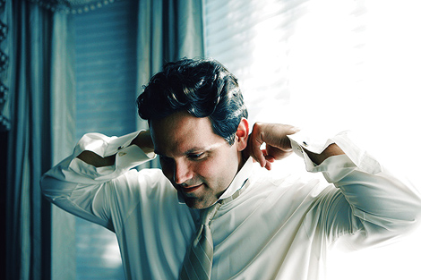 The groom fixes his tie in front of a window as he gets ready for his Los Angeles wedding