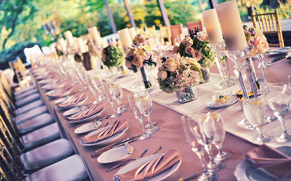 The long table is set beautifully for the wedding reception, and includes pink linens, pink flowers, and ivory candles to set the mood, photographed by Peter Van Beever