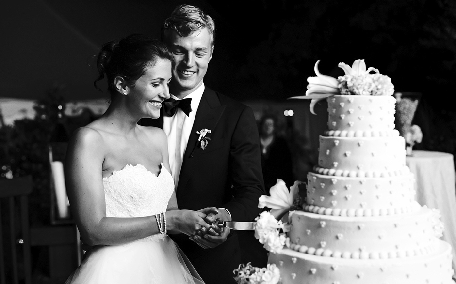 The bride and groom cut the cake outside on the deck at night at their Moorestown Field Club wedding reception, photography by Peter Van Beever