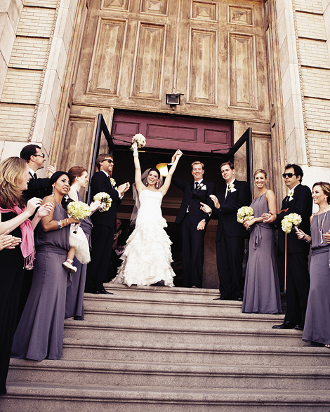 Everyone cheers as the bride and groom exit the door of the st rita cathedral and walk down the steps lined with their bridal party.