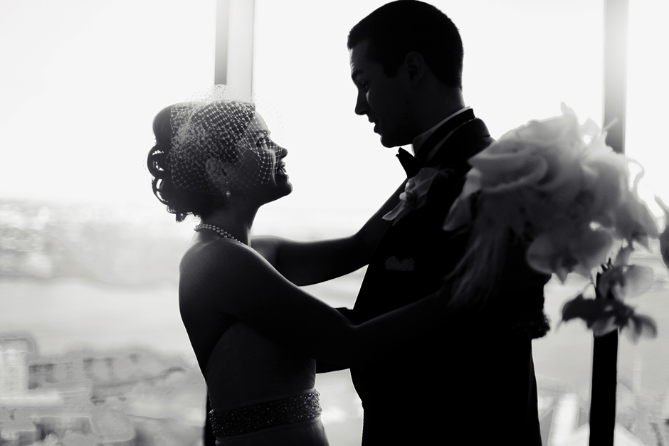 The bride and groom are partially silhouetted as they stand together in front of the Boston skyline at their wedding at the State Room, photographer:  Peter Van Beever